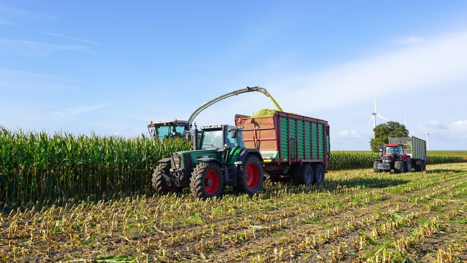 Harvesters collecting crops in a field with wind turbines beyond